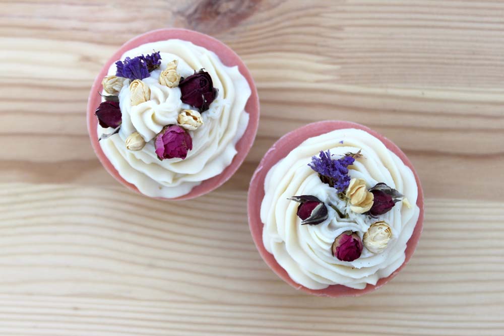 Zwei handgemachte Seifen in Cupcake-Form, verziert mit getrockneten Blüten, auf einem Holzuntergrund
