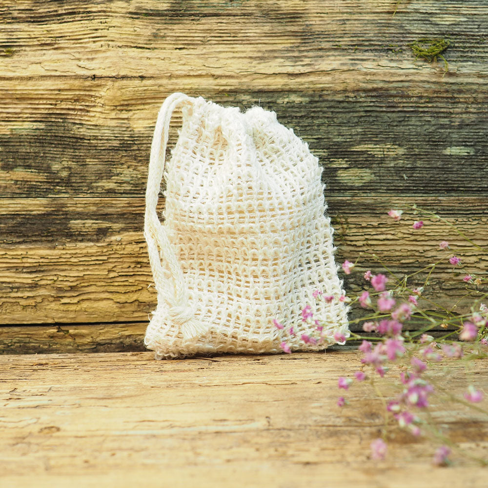 Seifensäckchen aus Naturfasern, aufrecht auf einem rustikalen Holztisch stehend, dekoriert mit rosa Blüten